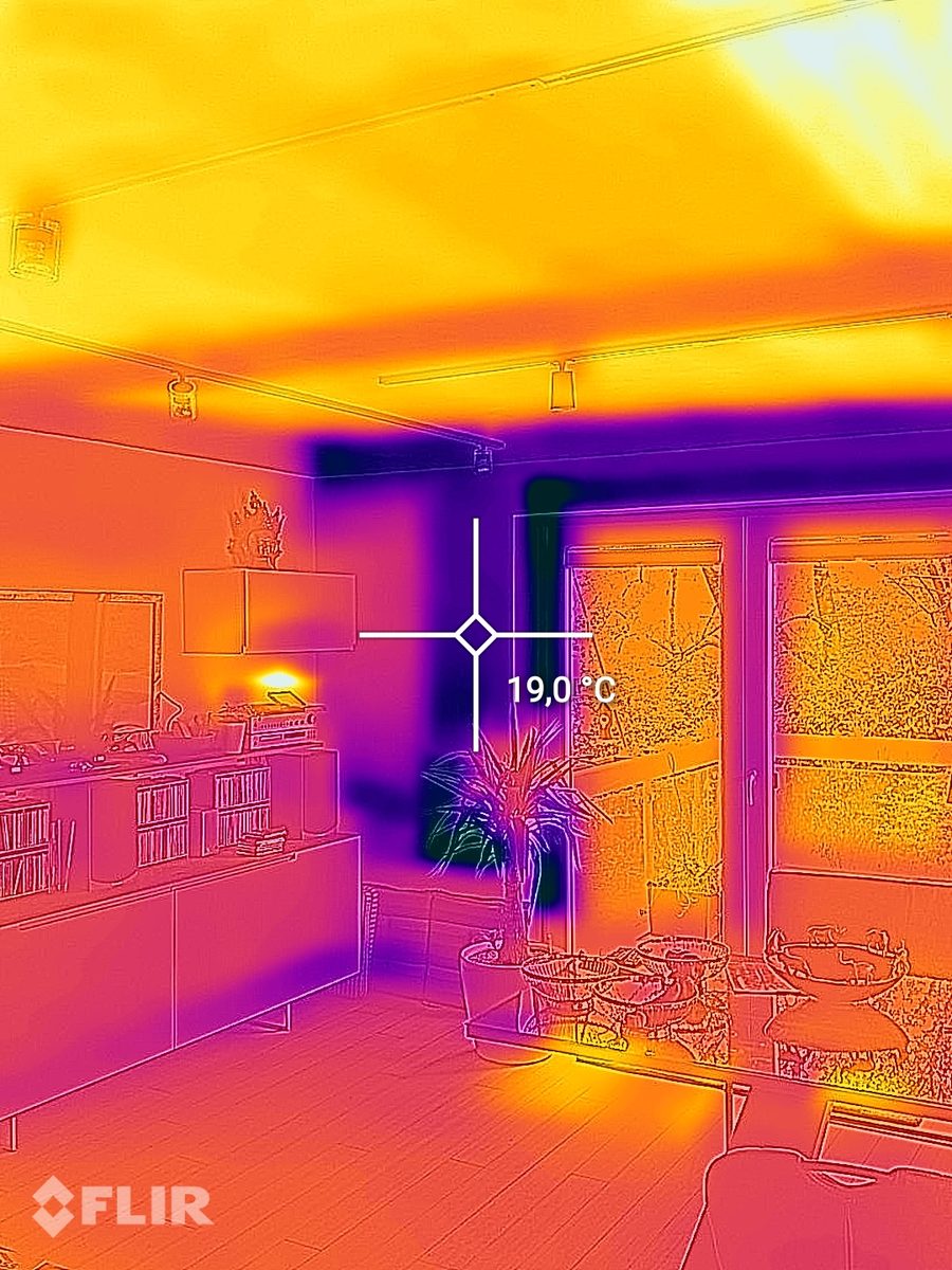 Warmtebeeld van een woonkamer met een warm plafond door de plafondverwarming en een meetpunt van 19,0 graden aan de buitenwand naast de terrasdeur.